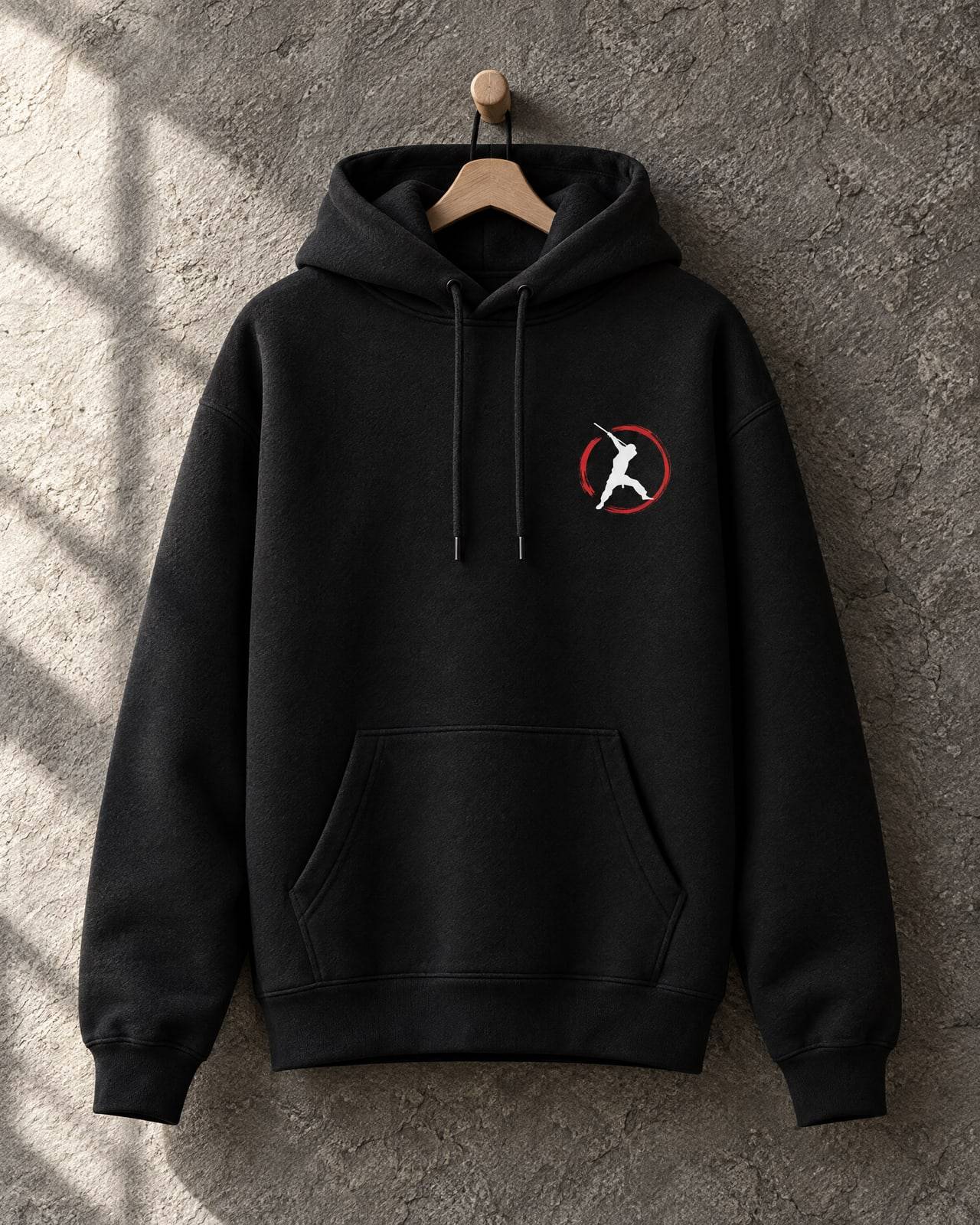 Concept mockup of a black hoodie on a wooden peg with a small ninja-in-a-red-ring print on the chest