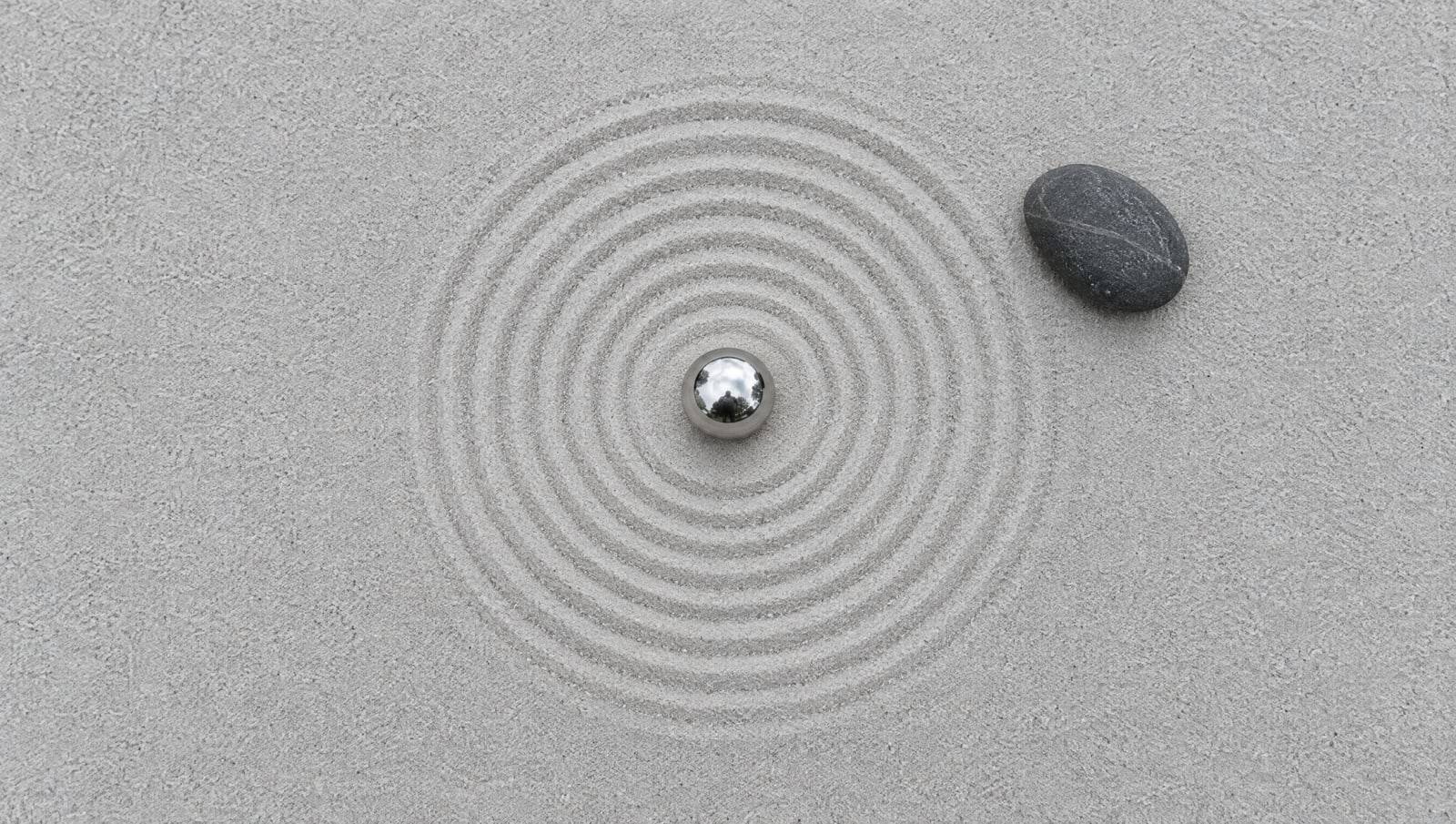 A steel pinball resting at the centre of raked circles in pale sand